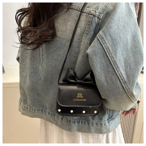 Detailed back view of a mini black polka dot crossbody bag with a bow on denim jacket