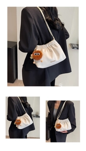 Detail view of cream pleated bucket bag with chain strap and cute plush monster charm