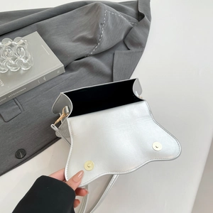 Close-up of silver crossbody bag featuring dual magnetic clasps and black interior lining