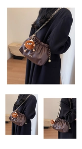 Detail view of dark brown bucket bag with gold chain and plush charm on black coat