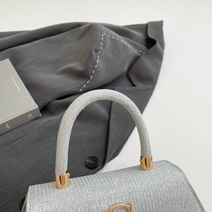 Macro detail of silver sequin handbag featuring golden metal logo and rigid top handle