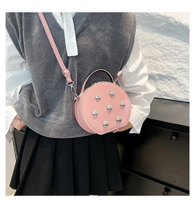 Bolso bandolera redondo rosa con tachuelas llevado por una modelo con atuendo casual chic