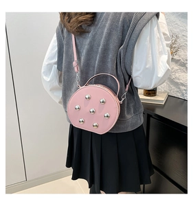 Detalle de un bolso bandolera rosa redondo con remaches plateados y acabado de cuero liso