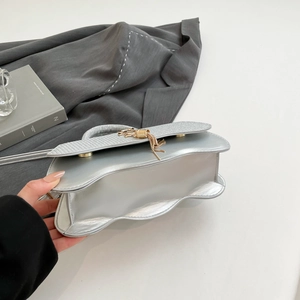 Detail of silver metallic handbag with unique wavy bottom and gold tassel ornament