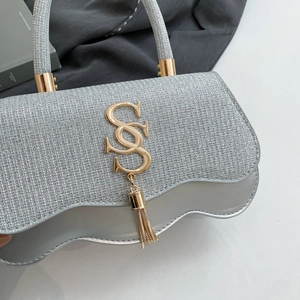 Detail of silver evening bag with glitter fabric, metallic logo, and tassel charm