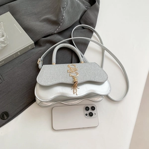 Detail of silver handbag with wavy edges, metallic SS logo and matching tassels