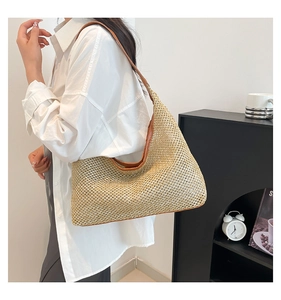Detail of hollow woven straw tote bag with brown leather trim and shoulder strap
