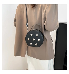 Detail van een zwarte ronde crossbodytas met zilveren studs op een kaki blazer outfit