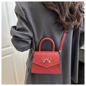 Detail of red mini crossbody bag with golden bow and leather texture on grey suit