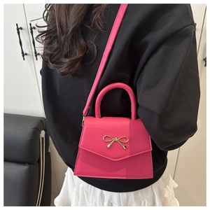 Magenta mini flap bag with golden bow hardware shown in a cross-body style view