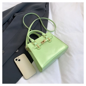 Top view of mint green handbag with gold hardware next to a gray suit on white fabric