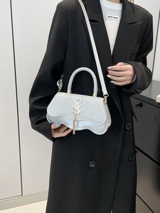 Silver sequin handbag with gold logo and tassels shown on a model in chic attire