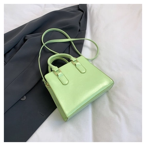 Detail view of a mint green crossbody bag with gold hardware on a gray background