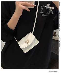 Close-up of white crossbody bag featuring a golden butterfly buckle and sleek flap design