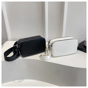 Detail of black and white litchi textured crossbody bags with dual zippers and wide straps