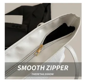 Detail view of smooth golden metal zipper and crocodile embossed texture on white tote bag