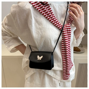 Detail of a black leather crossbody bag with a delicate gold and white butterfly clasp