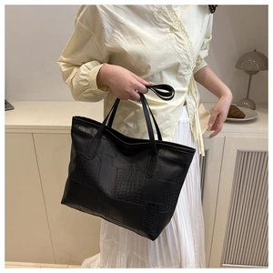 Detail of black tote bag featuring mixed textures of crocodile embossed and smooth leather
