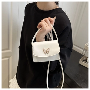 Detail of a mini white crossbody bag featuring a golden butterfly metal clasp decoration