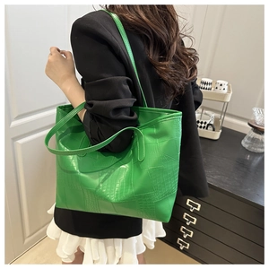 Detail of large green tote bag with crocodile texture on woman's shoulder