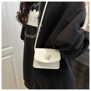 Close-up of white mini crossbody bag with golden butterfly detail on model outfit