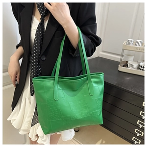 Detail of green tote bag featuring crocodile pattern texture and premium leather stitching