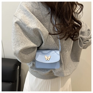 Detailed back view of a mini light blue crossbody bag with a golden butterfly on gray hoodie