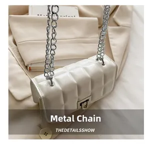 Detail of white quilted handbag with metallic chain and lock on a beige blazer