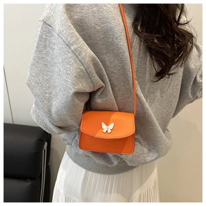 Detail of bright orange crossbody bag featuring a white butterfly ornament and slim strap