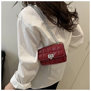 Close-up of red quilted crossbody bag with silver chain strap worn on a white shirt