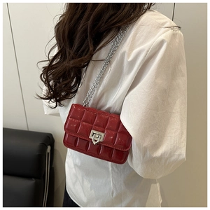 Detail of red patent leather crossbody bag with quilted texture and silver chain strap