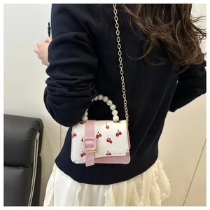 Detail of a mini cherry print crossbody bag featuring pearl handle and gold chain strap