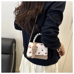Detail of cherry print mini bag with pearl handle and golden chain strap on model