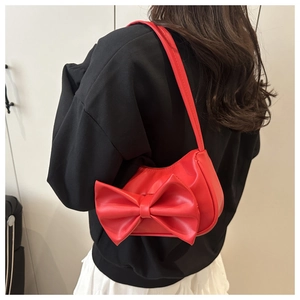 Detailed view of the red bow shoulder bag worn on the arm with a minimalist backdrop