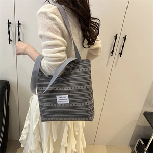 Large gray striped canvas tote bag with fashion tag worn by a model in casual style