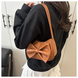 Close-up of brown leather armpit bag with large bow detail worn by model from behind