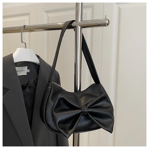 Detail of black faux leather shoulder bag featuring a large decorative 3D bow design
