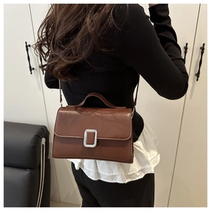 Sac bandoulière en cuir marron avec fermoir argenté porté par un mannequin en tenue chic