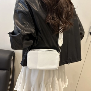 Minimalist white crossbody camera bag with wide fabric strap on a black leather jacket