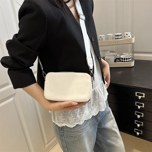 Modern white rectangular crossbody camera bag with wide fabric strap on a black blazer