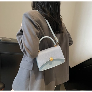 Close-up of light blue flap bag with textured fabric and golden magnetic buckle