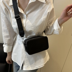 Minimalist black leather camera bag with dual zippers and adjustable wide fabric strap