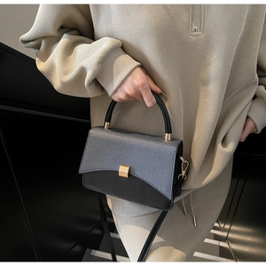 Detail of minimalist two-tone handbag with gold clasp and woven texture finish