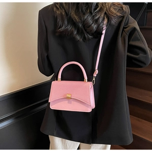 Detail of pink crossbody bag with mixed textures and gold buckle on a black blazer