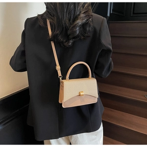 Close-up of a woven beige handbag with gold clasp carried by a model on stairs