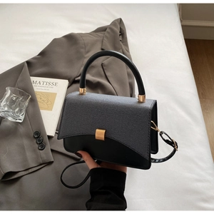 Detail of minimalist two-tone crossbody bag with elegant gold lock and textured flap