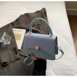 Detail of light blue textured crossbody bag with gold buckle and leather handle