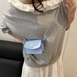 Light blue patent leather mini crossbody bag with a butterfly gold buckle on a model