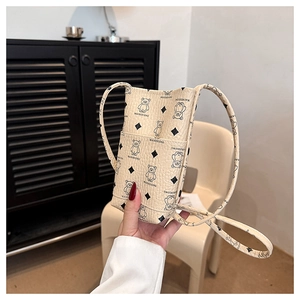 Detail view of mini cream crossbody bag with bear print held in hand for size context