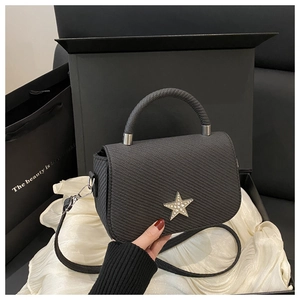 Detail of black woven saddle bag with gold star hardware on silk textured background